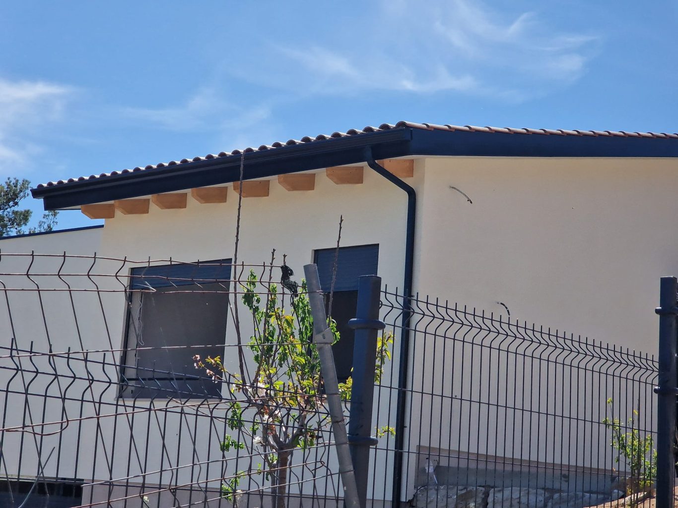 Casa moderna con techo de tejas, cercada y cielo azul despejado.