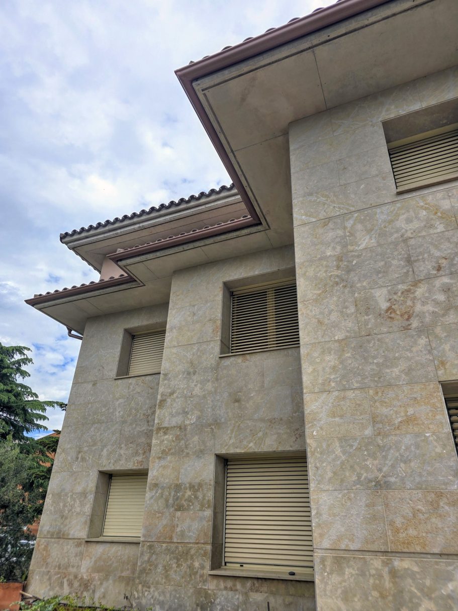 Fachada de un edificio de piedra con ventanas y un cielo nublado al fondo.