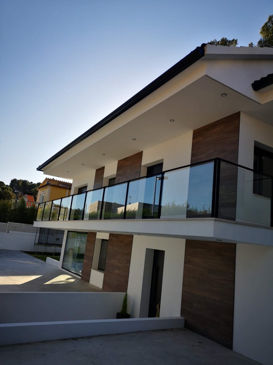 Casa moderna de dos pisos con balcón de vidrio y fachada de madera.