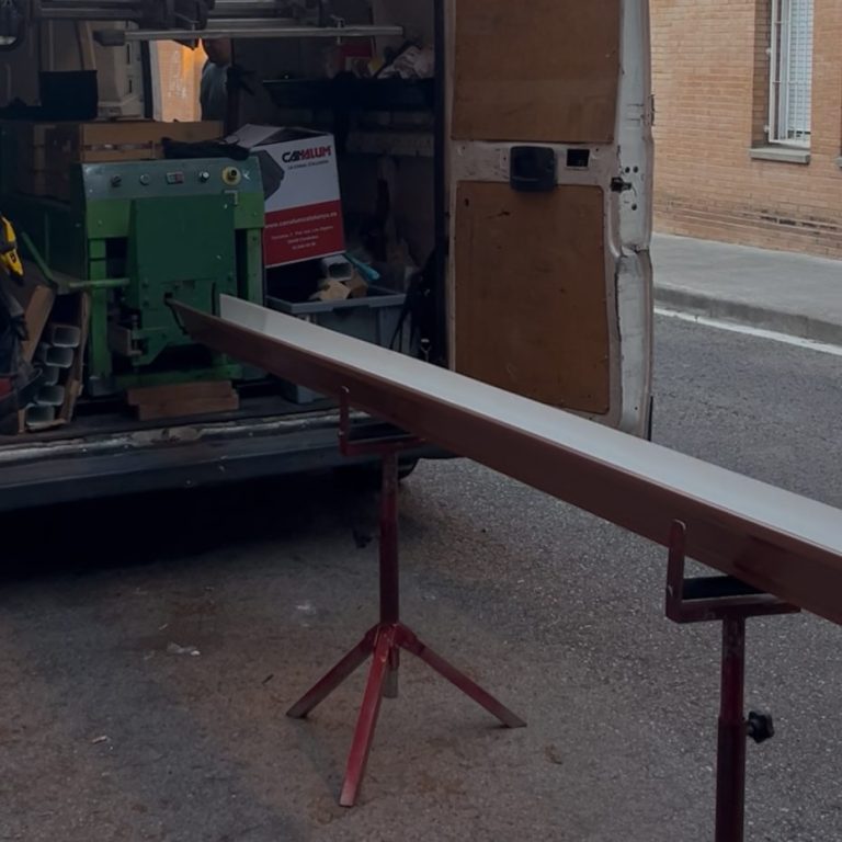 Una furgoneta con una máquina y una larga canal apoyada en un soporte.