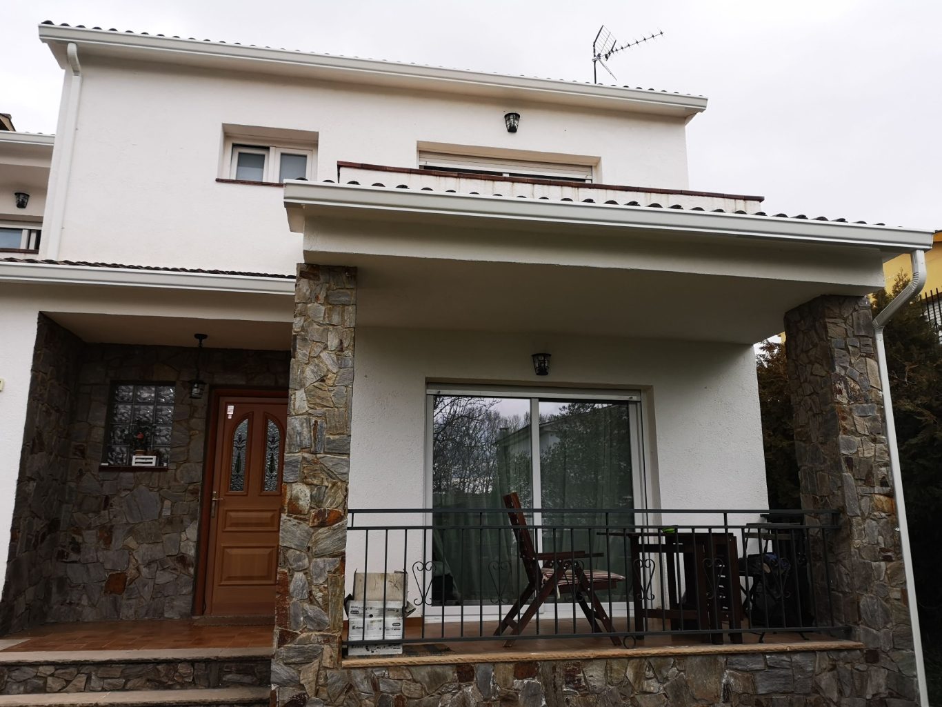 Casa de dos pisos con fachada de piedra y balcón, rodeada de un entorno tranquilo.