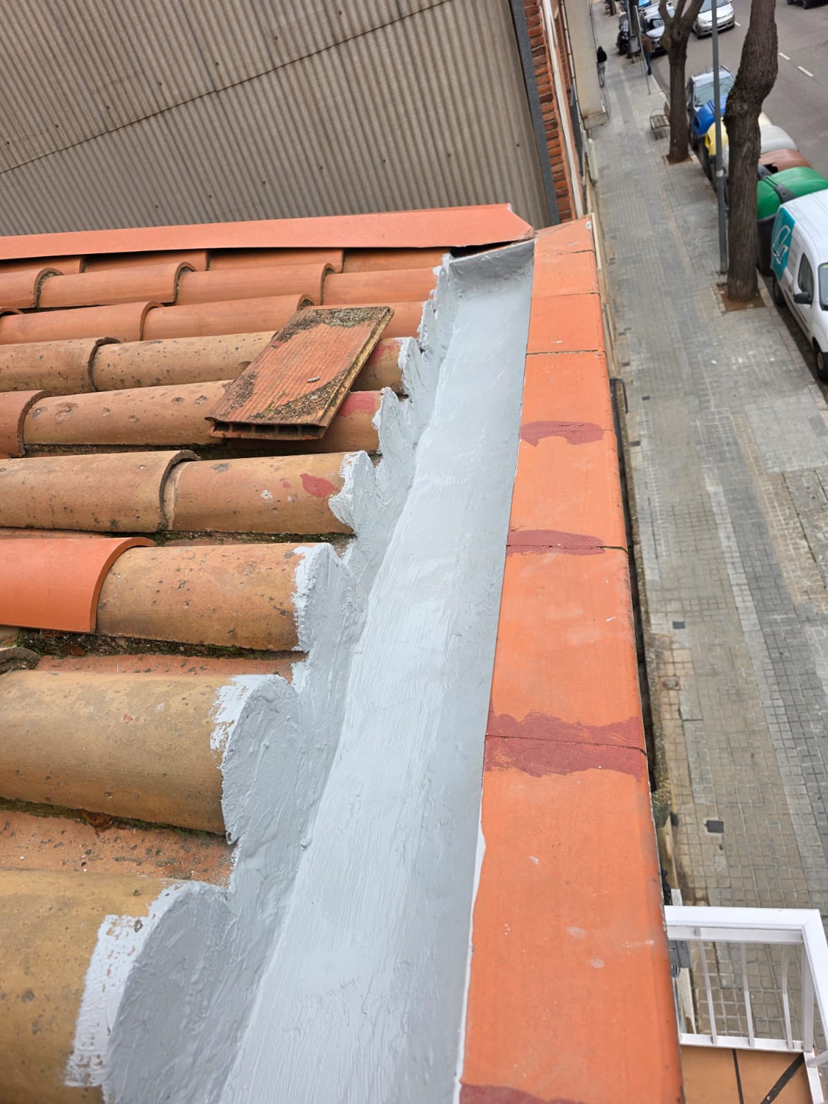Canalón de tejado con bordes de tejas, parcialmente dañado y pintado de gris.