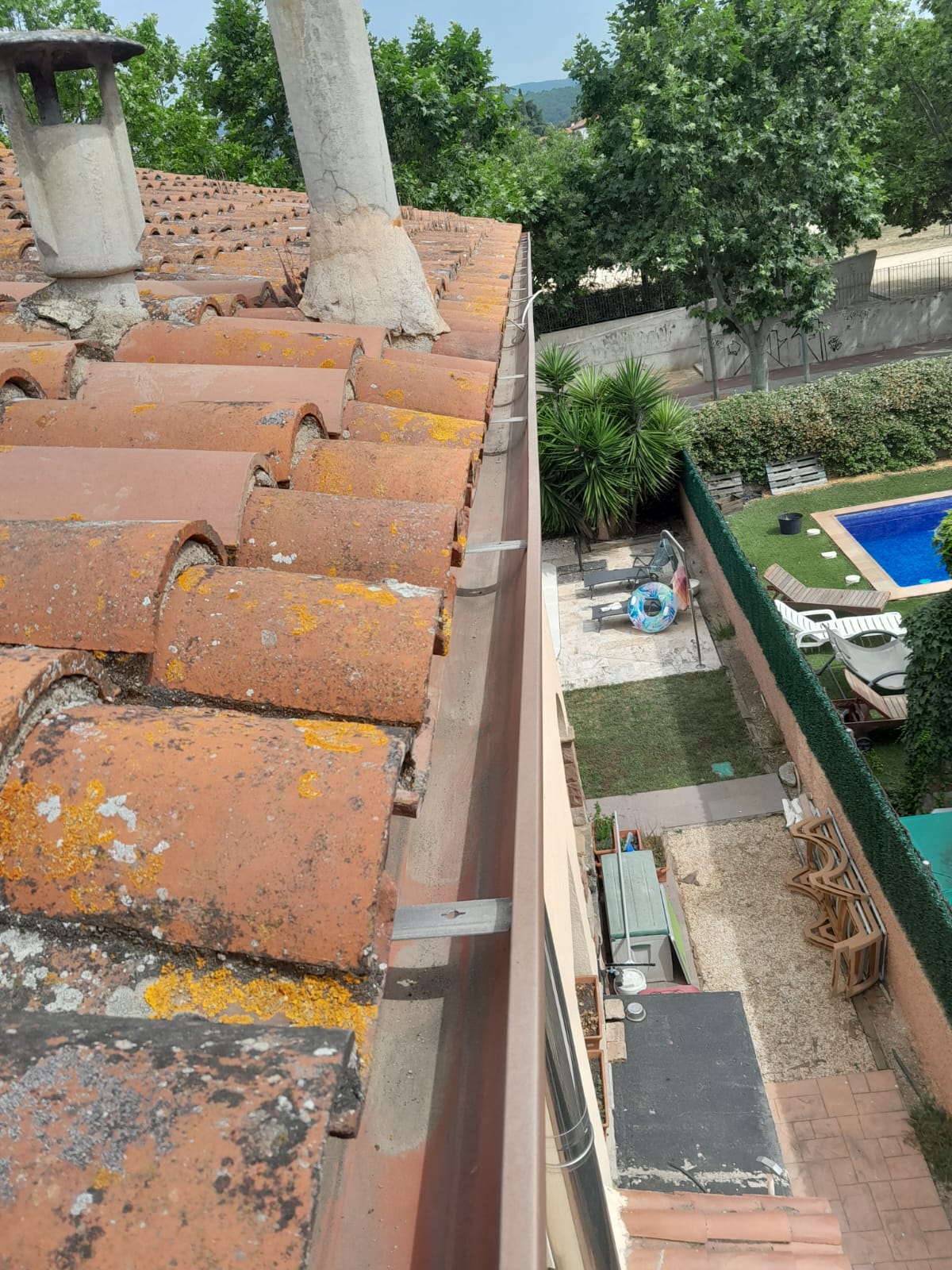 Vista aérea de un tejado de tejas y un jardín con piscina y mobiliario.