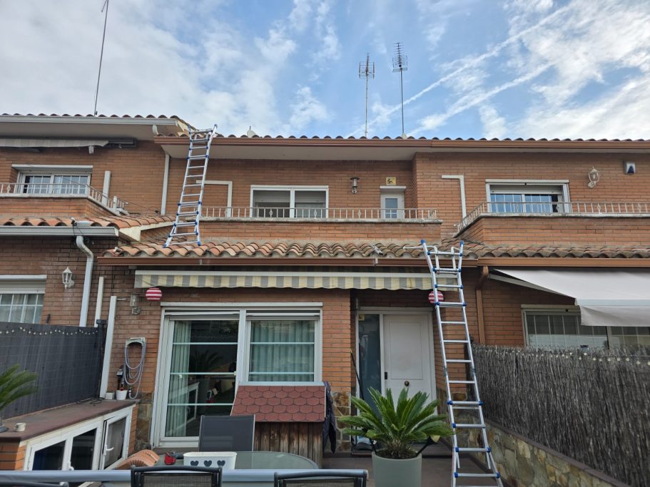 Casa de dos plantas con escaleras apoyadas en la fachada y plantas en el patio.