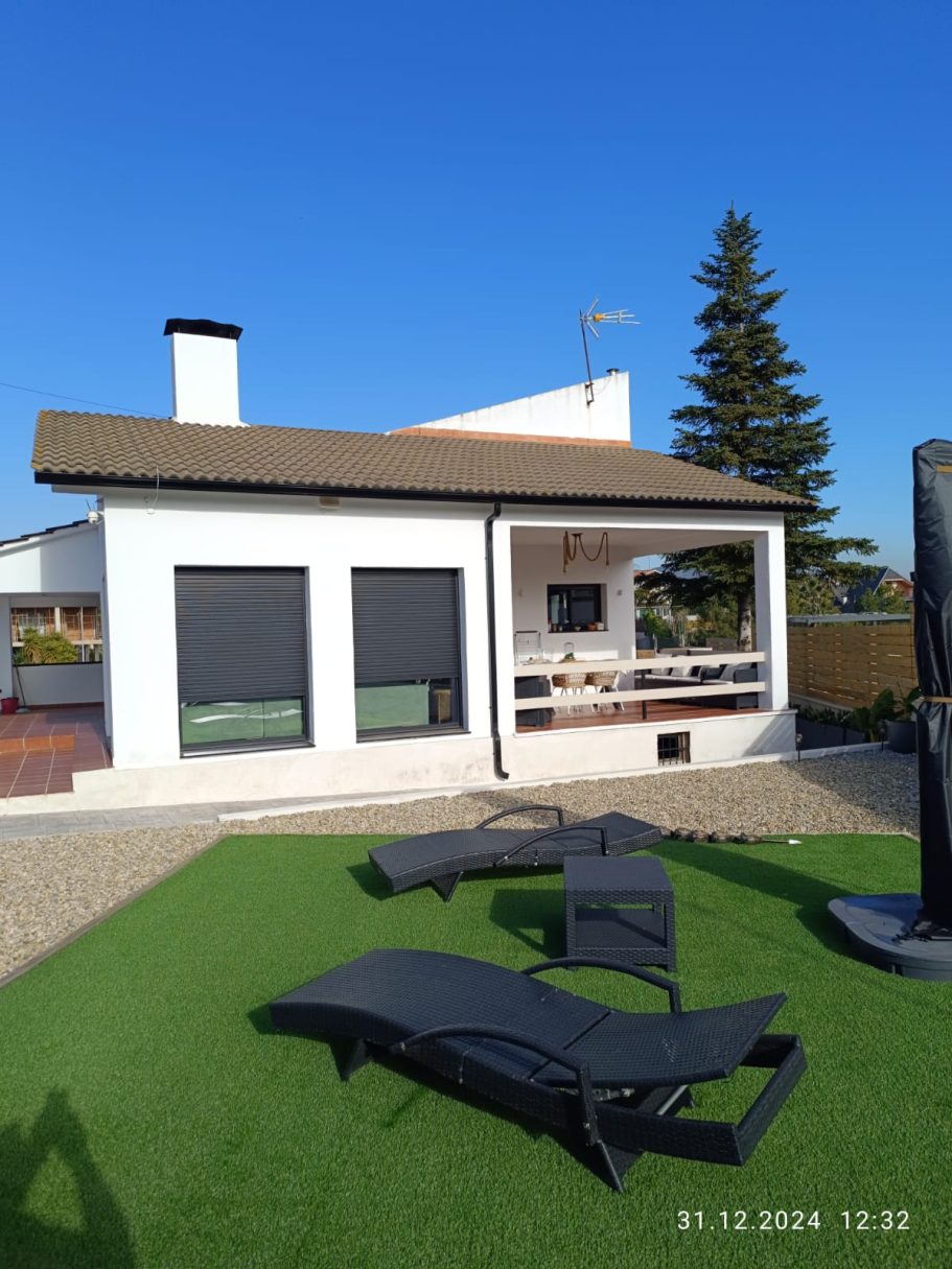 Casa moderna con jardín, tumbonas y cielo despejado.