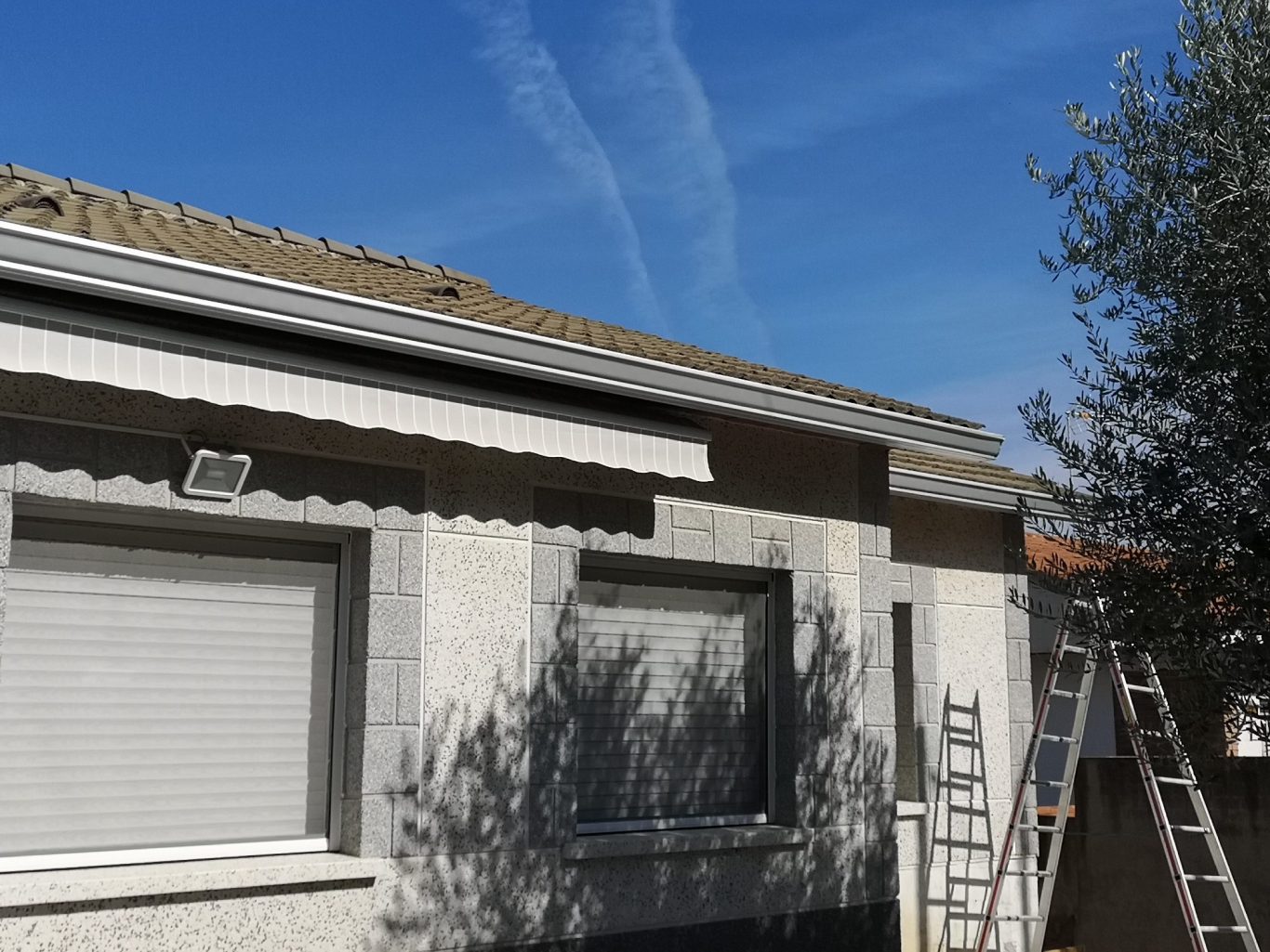 Fachada de una casa con un cielo azul y una escalera apoyada en el lateral.