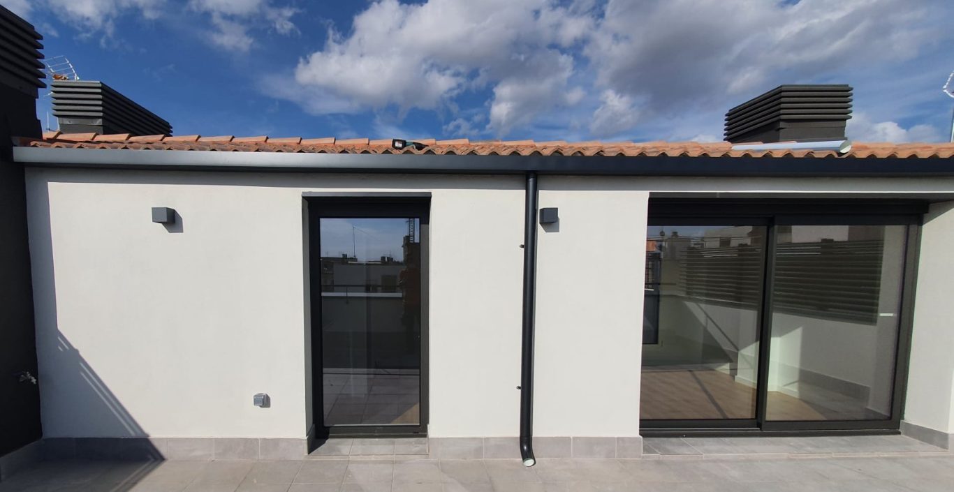 Fachada de una casa moderna con puertas y ventanas amplias, cielo parcialmente nublado.