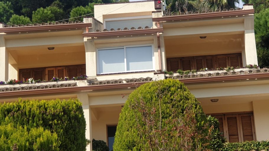 Casa de dos plantas con jardín, ventanas grandes y vegetación alrededor.