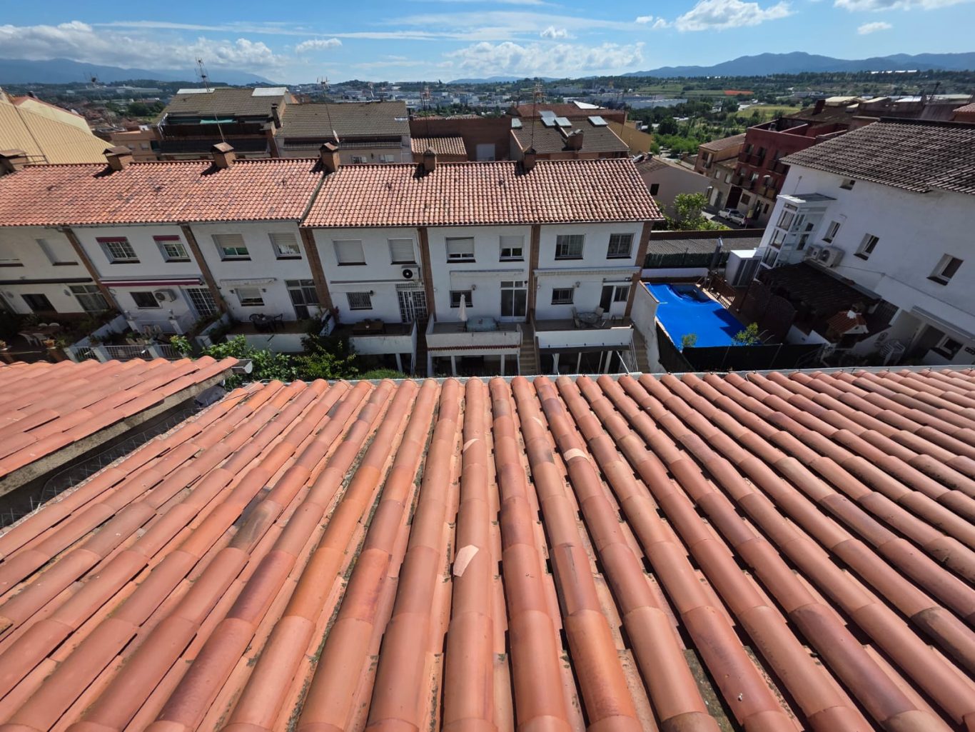 Vistas de techos de tejas y casas con fondo montañoso y cielo despejado.