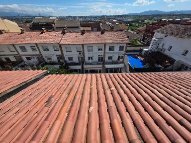 Vista desde un tejado, mostrando casas con techos de tejas y un cielo despejado.