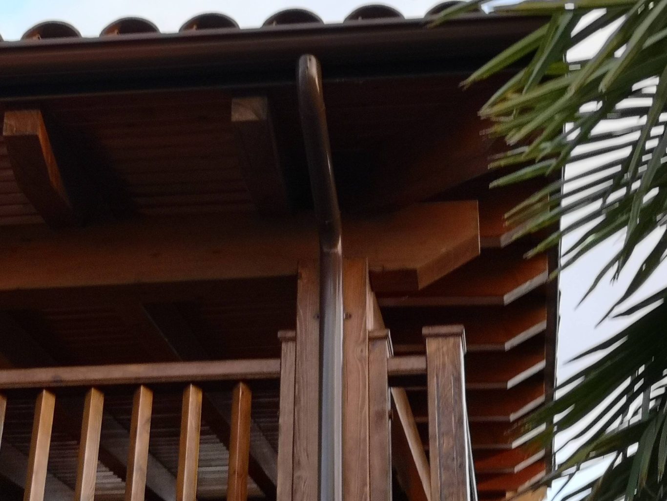 Esquina de un edificio de madera con barandillas y vegetación al fondo.