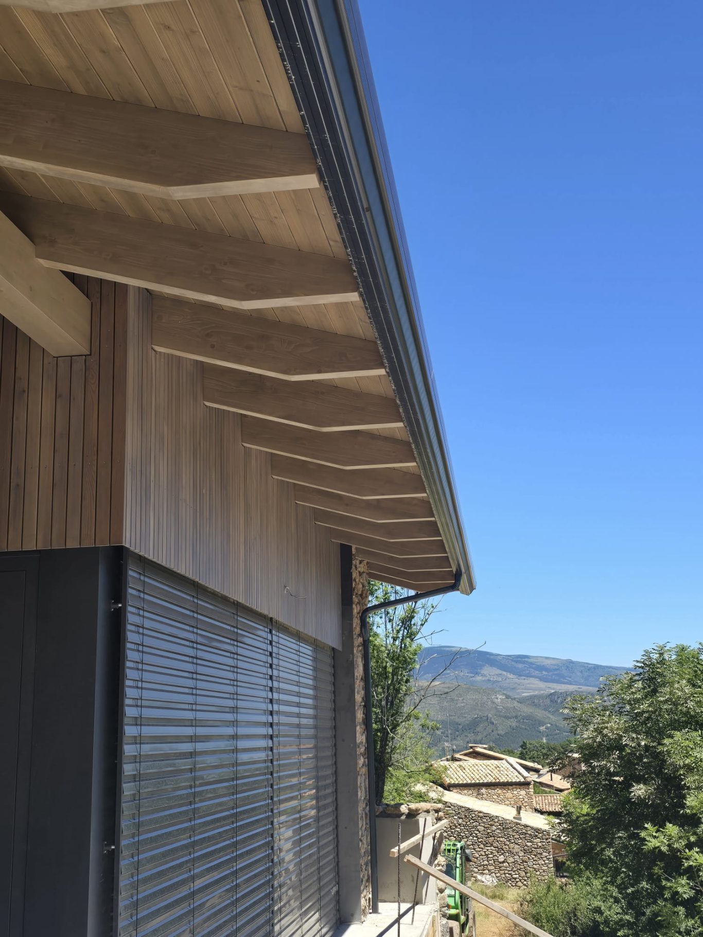 Techo en voladizo de madera sobre una construcción, con un cielo azul al fondo.